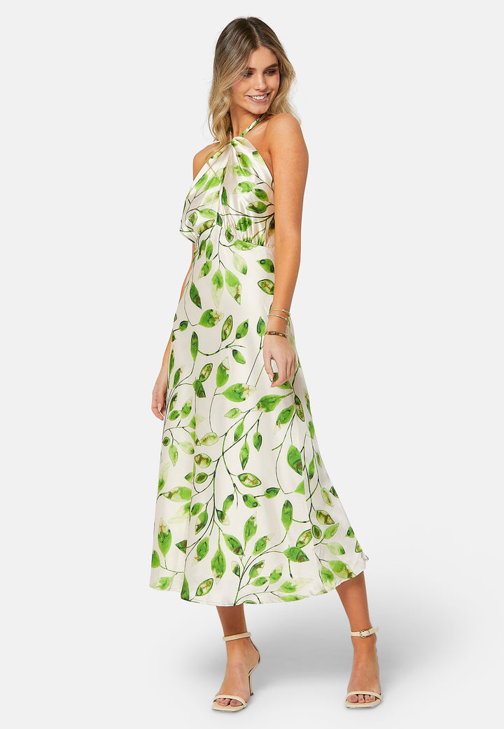 Introducing the Bronagh Leafy Print Dress: Elevate your summer wardrobe with this ankle-length halter neck dress, exquisitely designed for those special occasions. The dress features a bias-cut skirt that gracefully flows with every step, enhancing its feminine allure. The adjustable neck tie allows for a customizable fit, while the intricate knotted and twisted detail at the neckline adds an elegant touch to the halter design. 