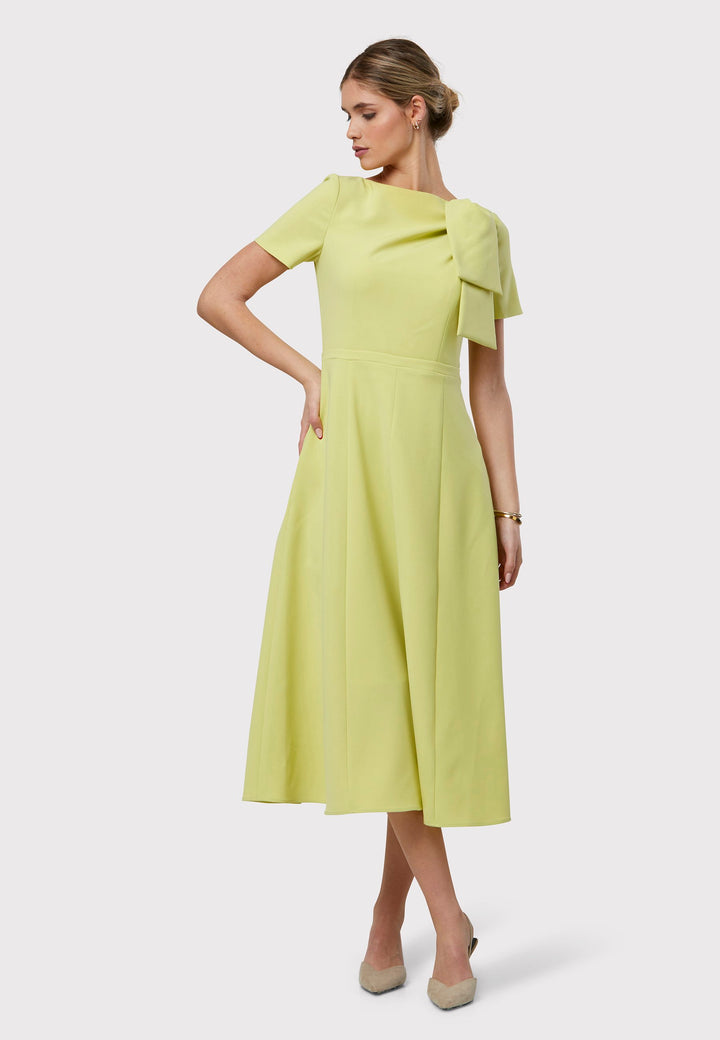 Introducing the Laoise Lime Dress, a refined statement piece designed exclusively for special occasions. Adorned with T-shirt-length sleeves and a meticulously fitted bodice, this dress features an elegant tie detail on the shoulder, creating a sophisticated pleat across the bust. The highlight of this ensemble is its fit-and-flare panelled skirt, gracefully cascading into a flattering A-line shape that exudes timeless elegance and movement.