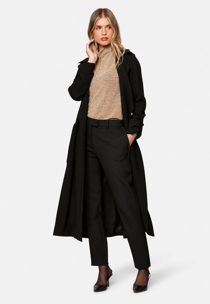 woman wearing black trench coat over beige knitwear and black pant
