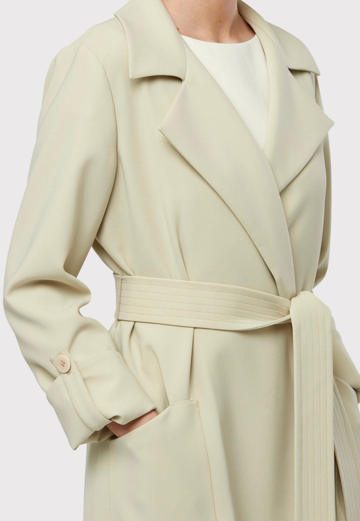 Lydiah captures the essence of sophisticated simplicity with its elegant design. This fluid trench coat features a neutral bone hue that radiates timeless appeal. It comes with a meticulously row-stitched, detachable belt that adds a touch of refinement, allowing you the flexibility to cinch it at the waist or wear it open for a relaxed look.