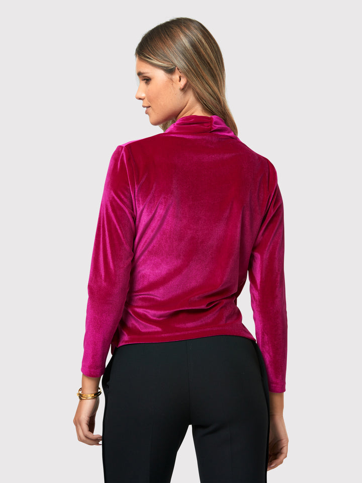 Introducing the Roxanne Fuchsia Velvet Top, an updated version of the beloved best-selling faux-wrap top. This captivating top boasts a sleek silhouette and a beautifully draped v-neckline, adding an elegant touch to your ensemble. Crafted from luxurious fuchsia stretch velvet, it radiates opulence and allure. With its hip-length cut and full-length sleeves, this top effortlessly combines comfort and style.
