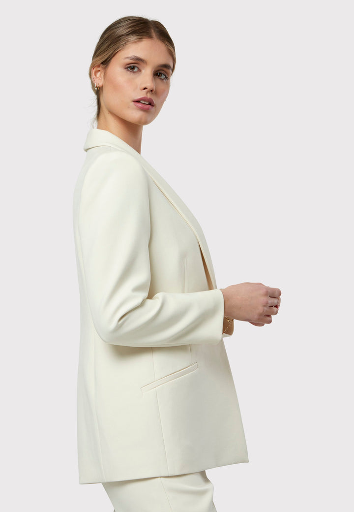 Darcie Ivory Jacket, a cornerstone for the discerning minimalist. This impeccably tailored tuxedo jacket exudes timeless elegance, featuring a seamless shawl collar and welt pockets. The semi-fitted silhouette is enhanced by a single button closure, ensuring a flattering and sophisticated look. Expertly crafted from our signature tricotine, it promises comfort and ease with just the right amount of stretch. For a polished tuxedo look, pair it with the matching Jill Ivory Trouser.