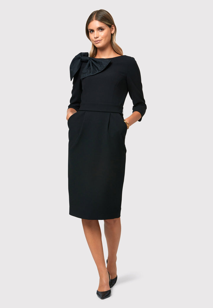 Introducing the Isadora Black Dress, a modern take on a classic Helen McAlinden design. With its exquisite craftsmanship and flattering silhouette, it accentuates your figure while offering practicality with pockets, a detachable belt, and a pencil skirt that elegantly falls to a mid-calf length. Adding to its versatility, the Isadora Black Dress features a detachable moire design bow that can be styled in multiple ways.