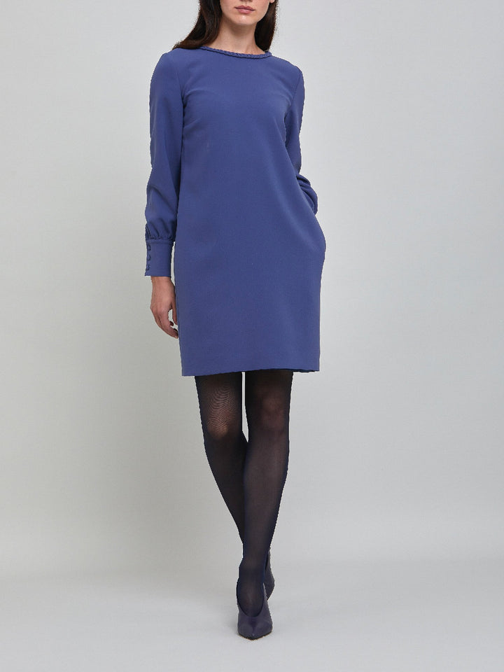 Rachel, a contemporary form-flattering shift dress. Crafted in a juniper blue tricotine with a hint of stretch. The round neck features an elegant plait trim & the easy-fitting sleeve softly gathers into a buttoned cuff. The skirt skims the knee. Work, Wine, or Dine in the Rachel Dress.