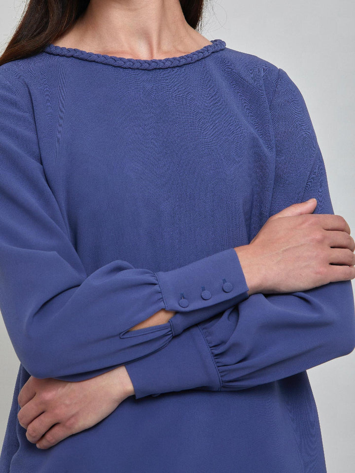 Rachel, a contemporary form-flattering shift dress. Crafted in a juniper blue tricotine with a hint of stretch. The round neck features an elegant plait trim & the easy-fitting sleeve softly gathers into a buttoned cuff. The skirt skims the knee. Work, Wine, or Dine in the Rachel Dress.
