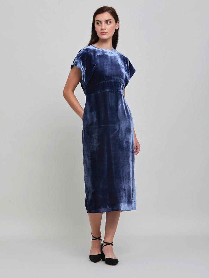 Occasionwear modernized. Meet the Shiv Juniper blue dress in Luxurious fluid velvet. An easy-fitting silhouette with side seam pockets falls to the mid-calf & features a side slit, dropped sleeves, and an elegant key-hole back neck detail. Attending a winter wedding? This is the dress for you.