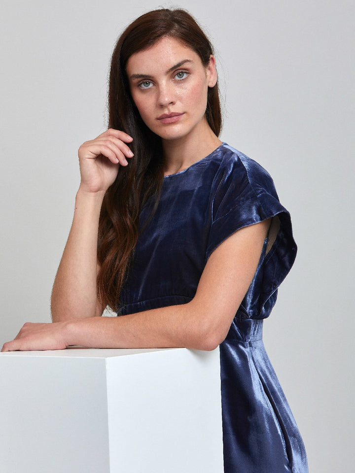 Occasionwear modernized. Meet the Shiv Juniper blue dress in Luxurious fluid velvet. An easy-fitting silhouette with side seam pockets falls to the mid-calf & features a side slit, dropped sleeves, and an elegant key-hole back neck detail. Attending a winter wedding? This is the dress for you.