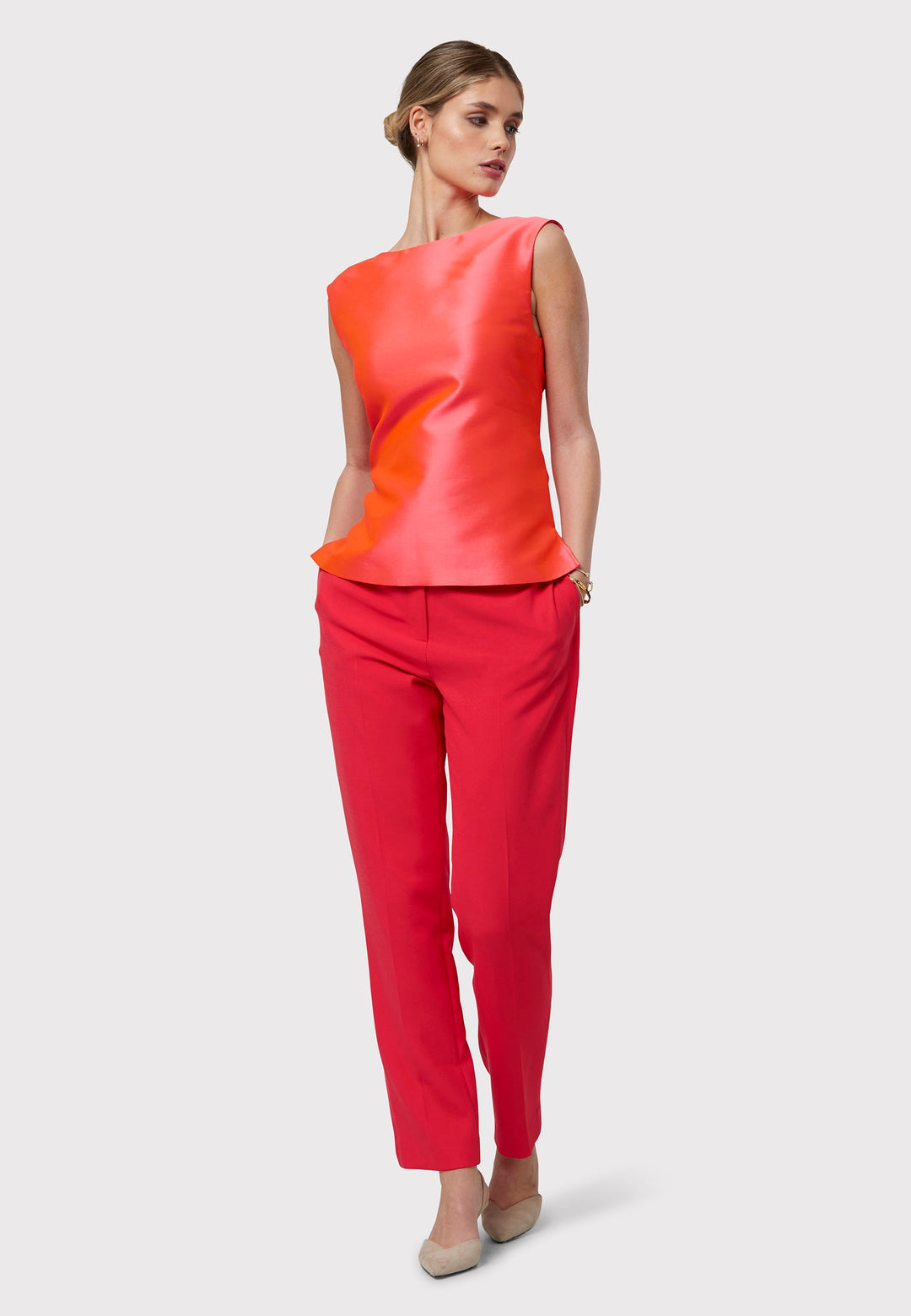 Stella Begonia Orange Top, a sleeveless foundation designed to complement our coordinating suiting or stand beautifully on its own. Boasting an iridescent sheen, this piece features two side slits and a central back zip. Embrace the vibrancy of spring with its captivating hue and playful elegance.