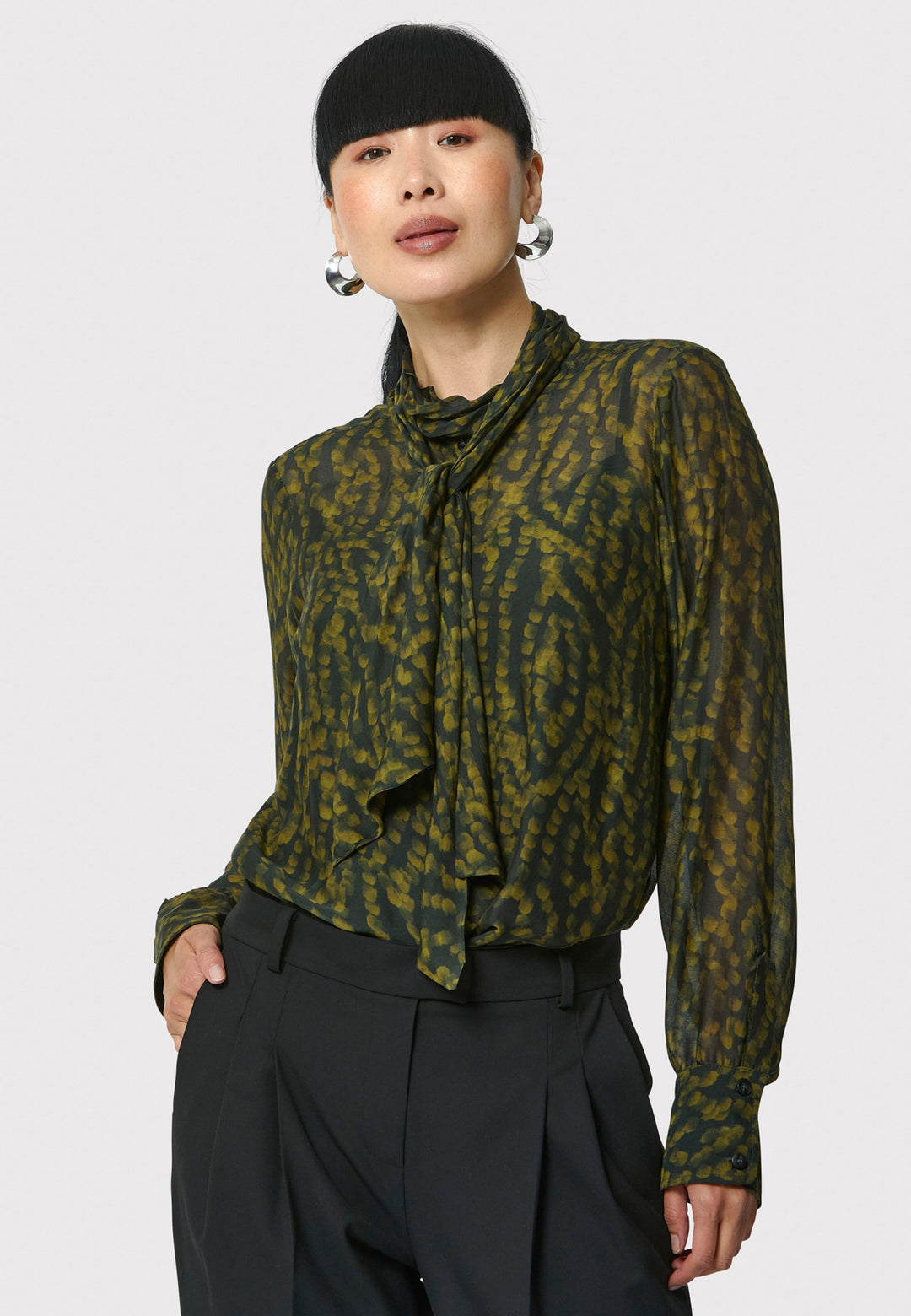 Anastasia Dark Green Forest Print Blouse, crafted from a luxurious viscose and silk blend, is perfect for your workwear wardrobe. This blouse features a round neckline, a chic pussy bow tie, and comes with a detachable slip. Pair it with the Marlena Sleeveless Chartreuse Green cashmere top, styled as a sweater vest, for a polished and professional look.