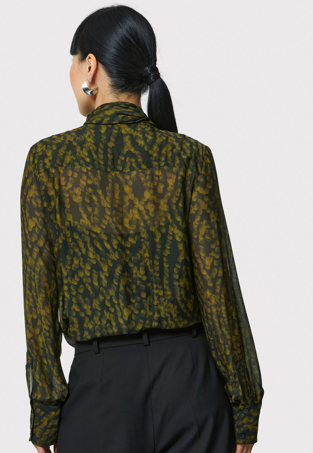 Anastasia Dark Green Forest Print Blouse, crafted from a luxurious viscose and silk blend, is perfect for your workwear wardrobe. This blouse features a round neckline, a chic pussy bow tie, and comes with a detachable slip. Pair it with the Marlena Sleeveless Chartreuse Green cashmere top, styled as a sweater vest, for a polished and professional look.