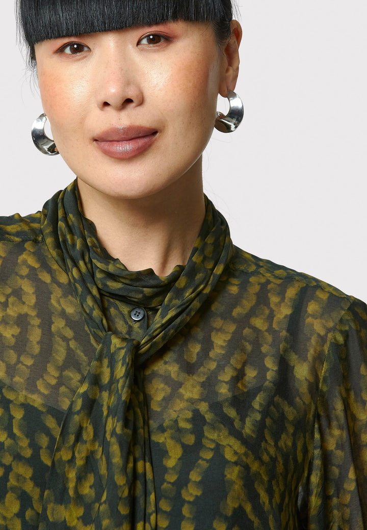 Anastasia Dark Green Forest Print Blouse, crafted from a luxurious viscose and silk blend, is perfect for your workwear wardrobe. This blouse features a round neckline, a chic pussy bow tie, and comes with a detachable slip. Pair it with the Marlena Sleeveless Chartreuse Green cashmere top, styled as a sweater vest, for a polished and professional look.