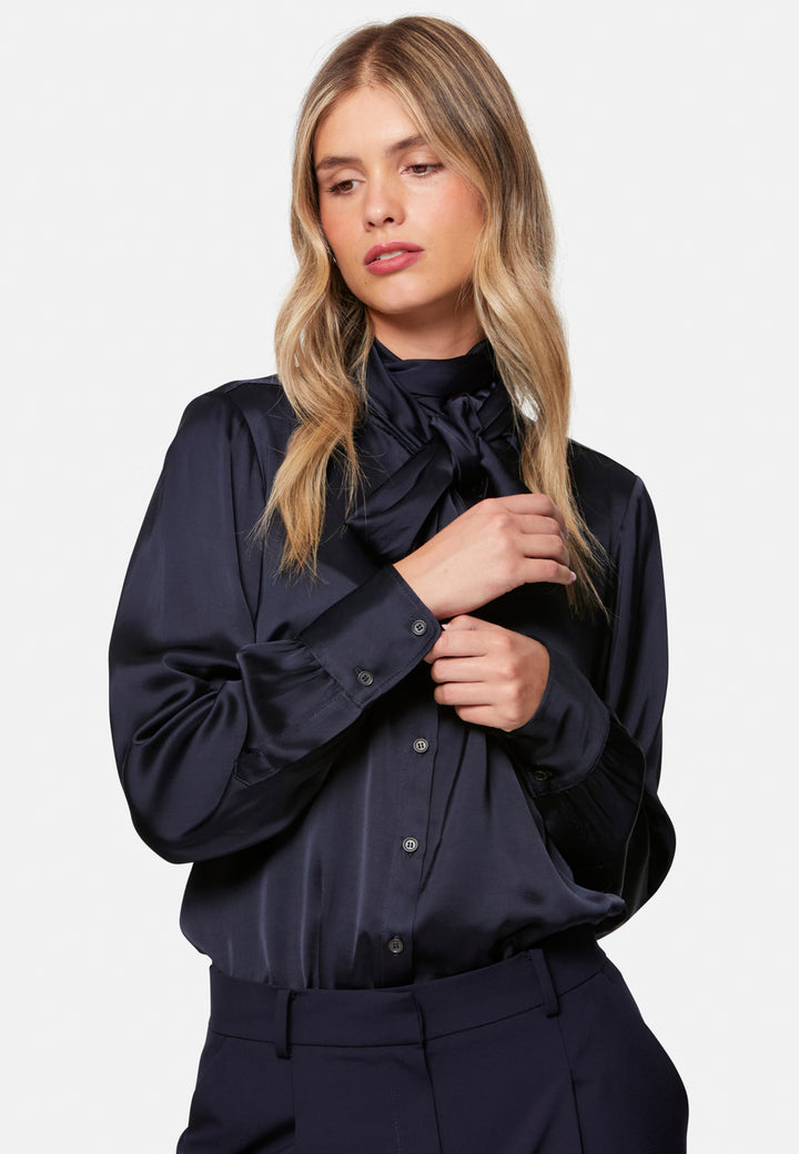 Woman wearing a dark blue satin blouse with a high bow collar on a white background