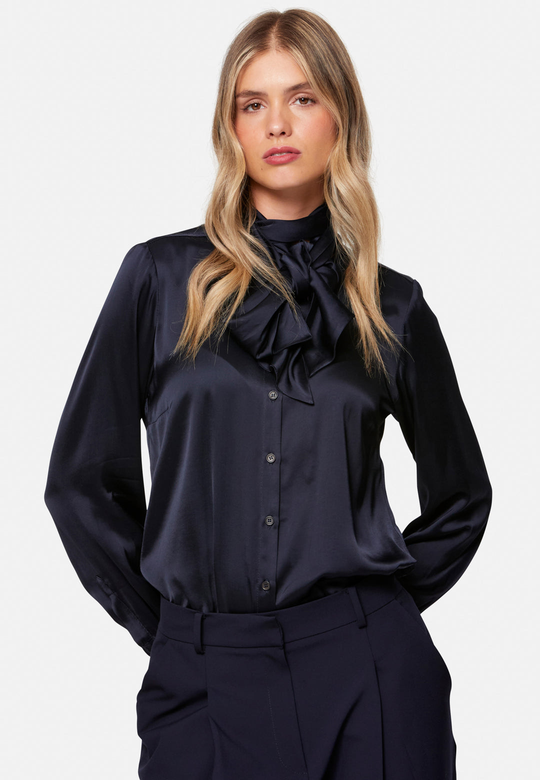 Woman wearing a navy blouse with a high bow collar against a white background