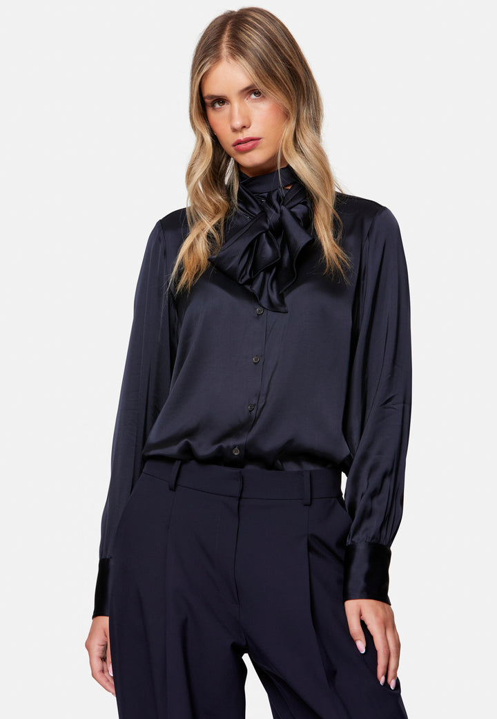 Woman wearing a dark blue blouse with a large bow and matching pants on a white background