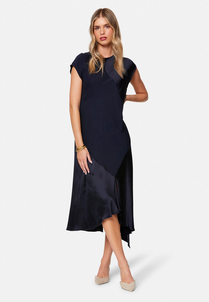 Carmin, the modern occasion dress with quiet drama. Cut from fluid, silk-touch satin in deep navy, it skims rather than clings, with a jewel neckline. Bias-cut panels and an asymmetric handkerchief hem add interest, while cap sleeves offer extra coverage. Style it with barely-there heels for evening, or a sharp blazer for city events.
