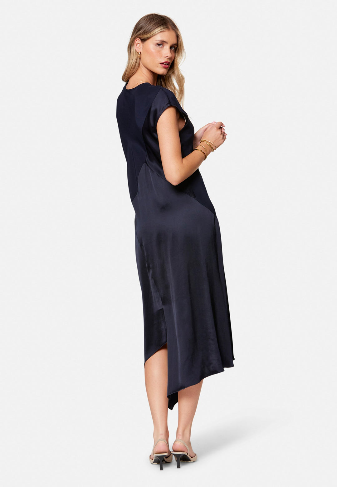 Carmin, the modern occasion dress with quiet drama. Cut from fluid, silk-touch satin in deep navy, it skims rather than clings, with a jewel neckline. Bias-cut panels and an asymmetric handkerchief hem add interest, while cap sleeves offer extra coverage. Style it with barely-there heels for evening, or a sharp blazer for city events.