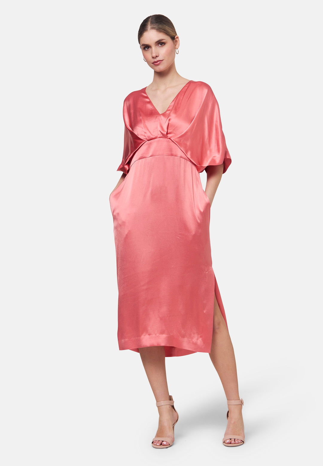 Eabha, the coral rose dress with quiet glamour. Cut from fluid, silk-touch satin, it frames the neckline with a gentle V and draped kimono sleeves, then gathers into under-bust pleats that flatter the waistline. The column midi skirt skims beautifully with discreet side seam pockets and slits for ease, finished with a neat keyhole back. Just add barely-there heels and gold jewellery.