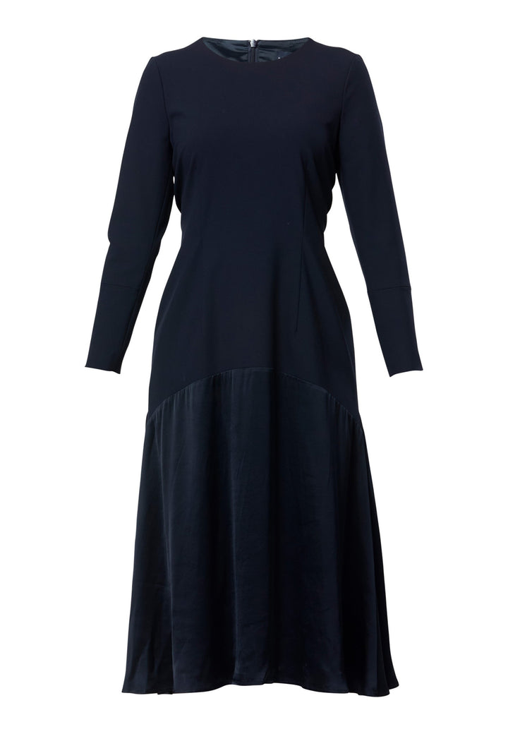 Kristy, a modern take on the dropped waist. Cut from plain-weave worsted navy fabric with a touch of stretch, the dress contrasts with a fluid viscose satin skirt that flows softly from the low hip. Designed with a clean round neckline, long fitted sleeves, a dropped waistline and a gently flared midi skirt that falls to mid-calf. The tonal fabric pairing creates subtle dimension, while the detachable satin scarf/belt can be cinched at the waist or draped elegantly around the neck. 