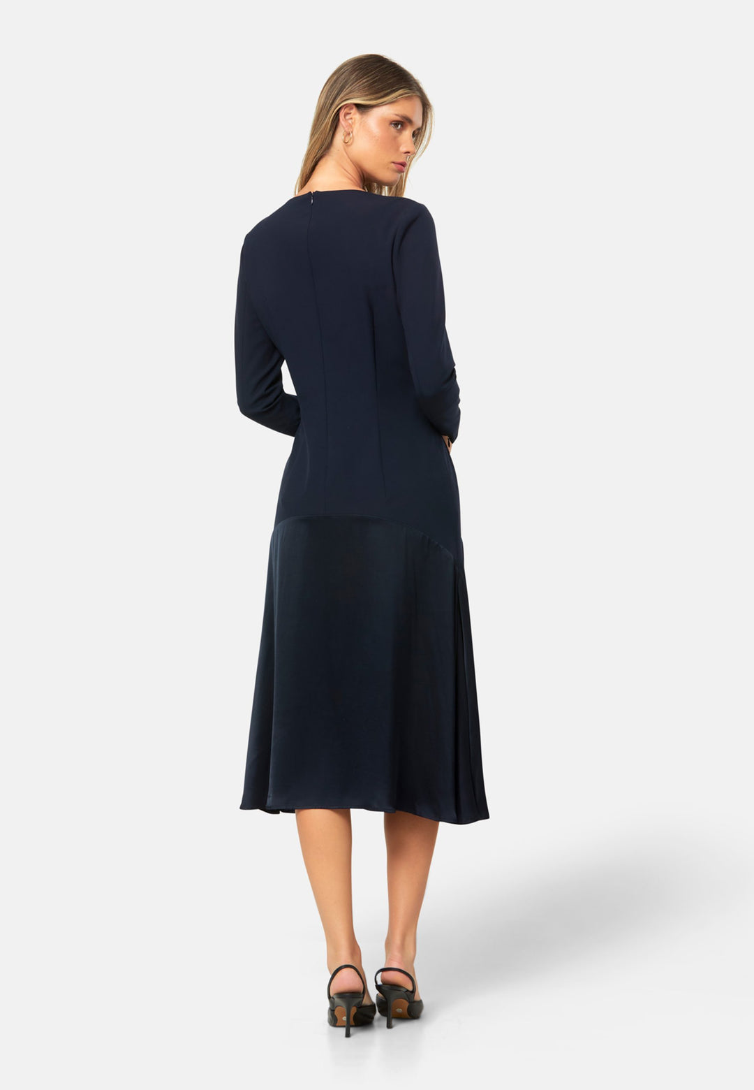 Kristy, a modern take on the dropped waist. Cut from plain-weave worsted navy fabric with a touch of stretch, the dress contrasts with a fluid viscose satin skirt that flows softly from the low hip. Designed with a clean round neckline, long fitted sleeves, a dropped waistline and a gently flared midi skirt that falls to mid-calf. The tonal fabric pairing creates subtle dimension, while the detachable satin scarf/belt can be cinched at the waist or draped elegantly around the neck. 