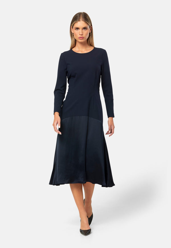 Kristy, a modern take on the dropped waist. Cut from plain-weave worsted navy fabric with a touch of stretch, the dress contrasts with a fluid viscose satin skirt that flows softly from the low hip. Designed with a clean round neckline, long fitted sleeves, a dropped waistline and a gently flared midi skirt that falls to mid-calf. The tonal fabric pairing creates subtle dimension, while the detachable satin scarf/belt can be cinched at the waist or draped elegantly around the neck. 