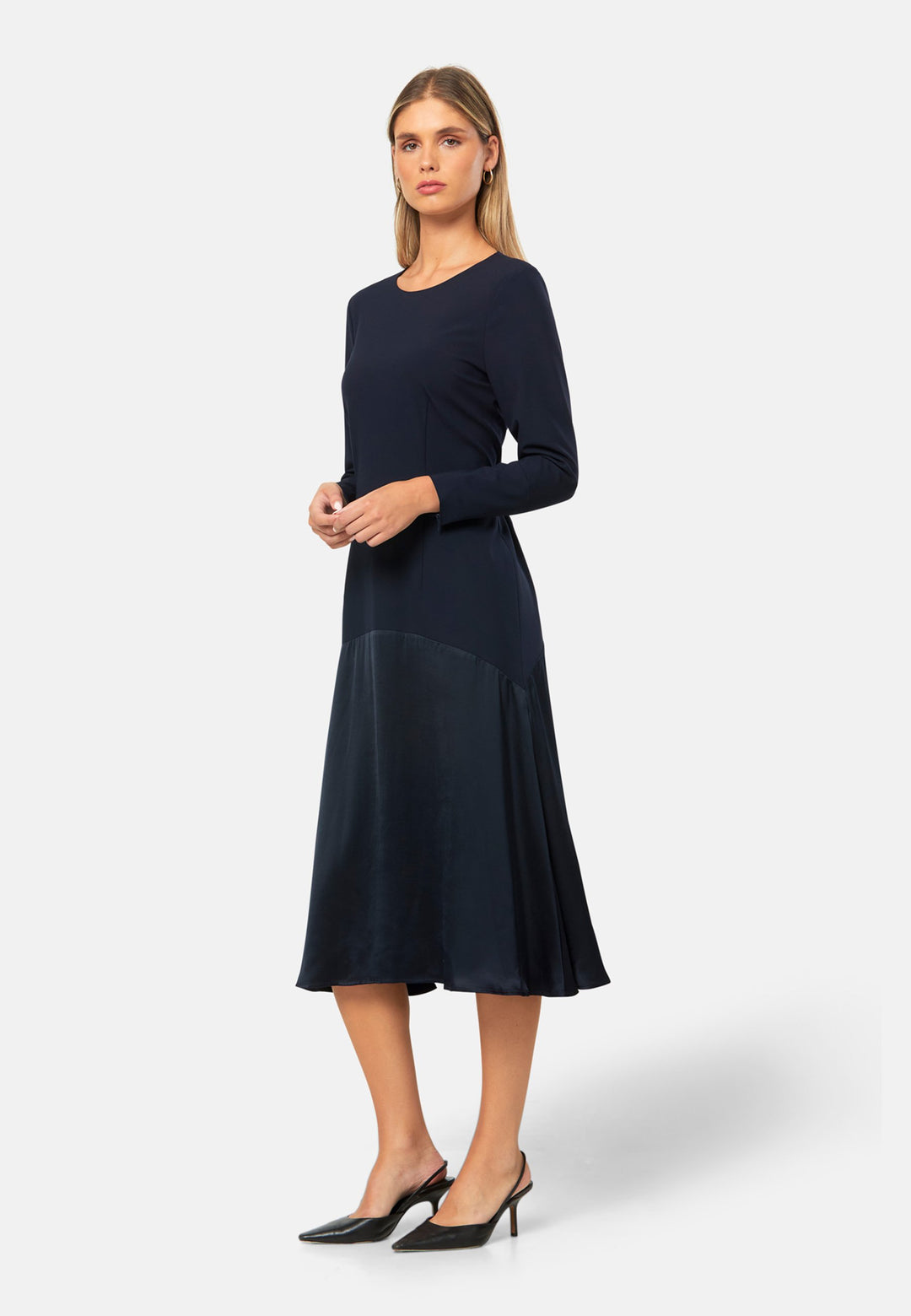 Kristy, a modern take on the dropped waist. Cut from plain-weave worsted navy fabric with a touch of stretch, the dress contrasts with a fluid viscose satin skirt that flows softly from the low hip. Designed with a clean round neckline, long fitted sleeves, a dropped waistline and a gently flared midi skirt that falls to mid-calf. The tonal fabric pairing creates subtle dimension, while the detachable satin scarf/belt can be cinched at the waist or draped elegantly around the neck. 