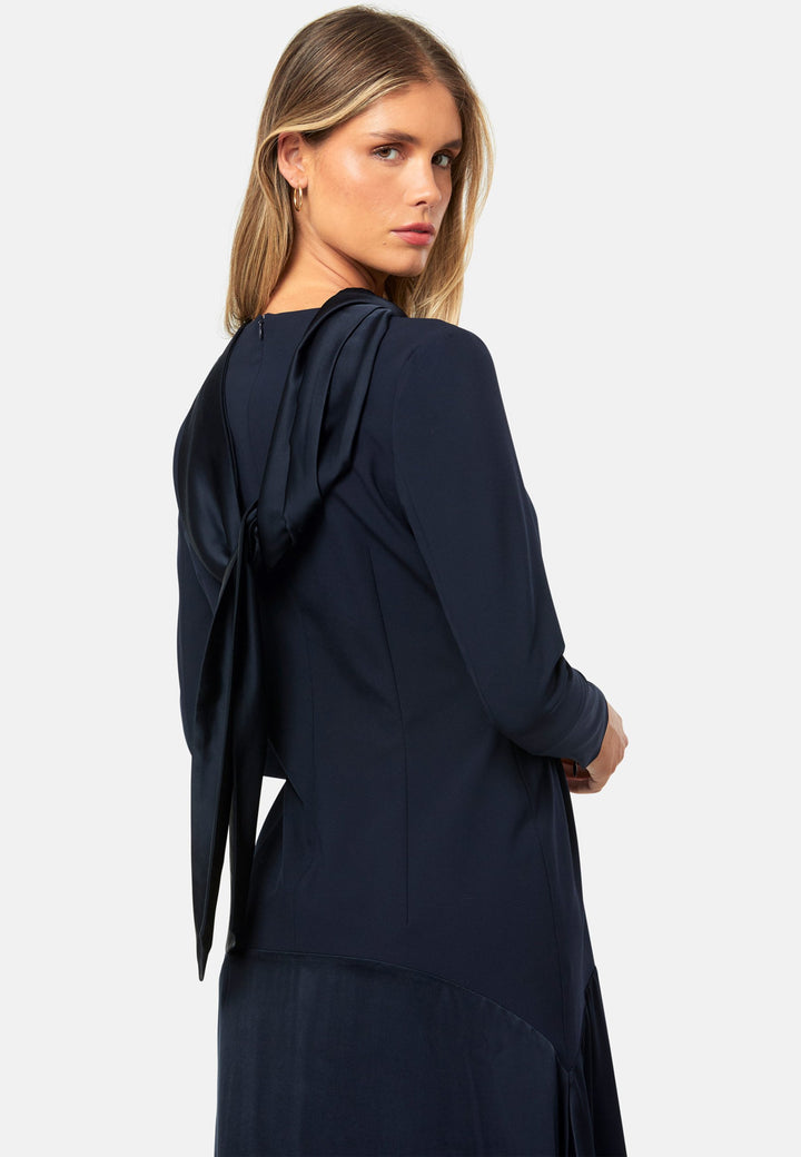 Kristy, a modern take on the dropped waist. Cut from plain-weave worsted navy fabric with a touch of stretch, the dress contrasts with a fluid viscose satin skirt that flows softly from the low hip. Designed with a clean round neckline, long fitted sleeves, a dropped waistline and a gently flared midi skirt that falls to mid-calf. The tonal fabric pairing creates subtle dimension, while the detachable satin scarf/belt can be cinched at the waist or draped elegantly around the neck. 