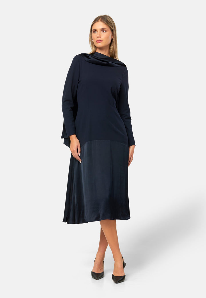Kristy, a modern take on the dropped waist. Cut from plain-weave worsted navy fabric with a touch of stretch, the dress contrasts with a fluid viscose satin skirt that flows softly from the low hip. Designed with a clean round neckline, long fitted sleeves, a dropped waistline and a gently flared midi skirt that falls to mid-calf. The tonal fabric pairing creates subtle dimension, while the detachable satin scarf/belt can be cinched at the waist or draped elegantly around the neck. 