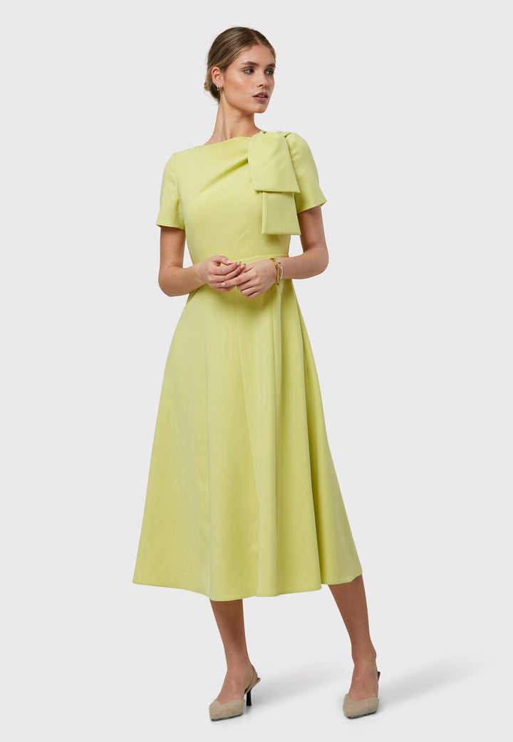 Introducing the Laoise Lime Dress, a refined statement piece designed exclusively for special occasions. Adorned with T-shirt-length sleeves and a meticulously fitted bodice, this dress features an elegant tie detail on the shoulder, creating a sophisticated pleat across the bust. The highlight of this ensemble is its fit-and-flare panelled skirt, gracefully cascading into a flattering A-line shape that exudes timeless elegance and movement.