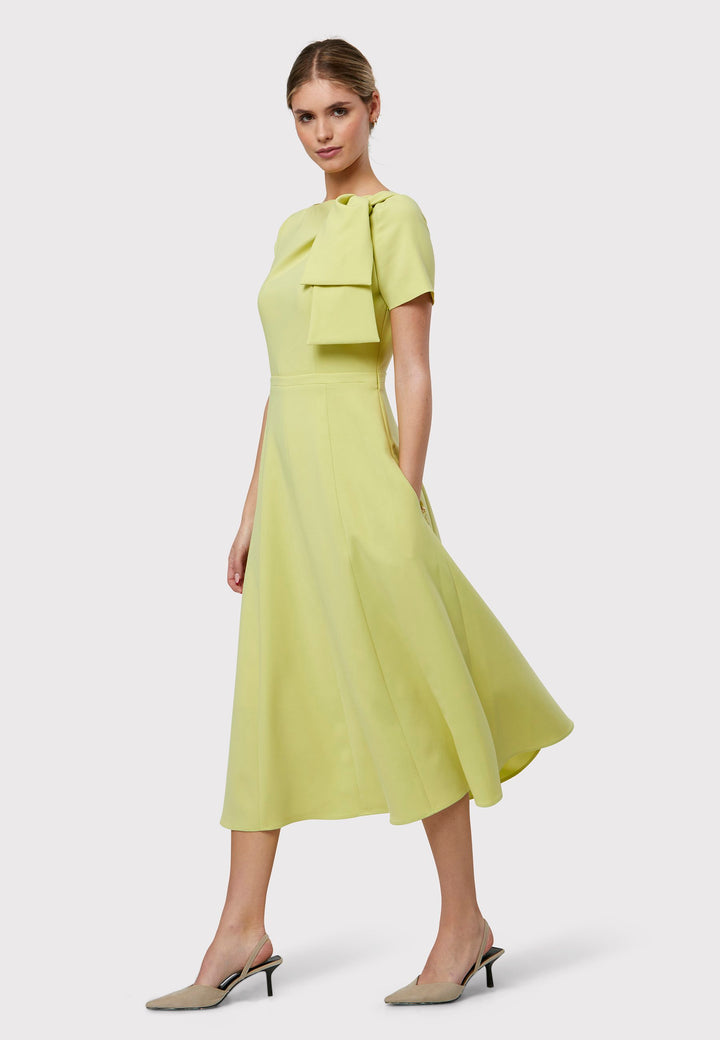 Introducing the Laoise Lime Dress, a refined statement piece designed exclusively for special occasions. Adorned with T-shirt-length sleeves and a meticulously fitted bodice, this dress features an elegant tie detail on the shoulder, creating a sophisticated pleat across the bust. The highlight of this ensemble is its fit-and-flare panelled skirt, gracefully cascading into a flattering A-line shape that exudes timeless elegance and movement.