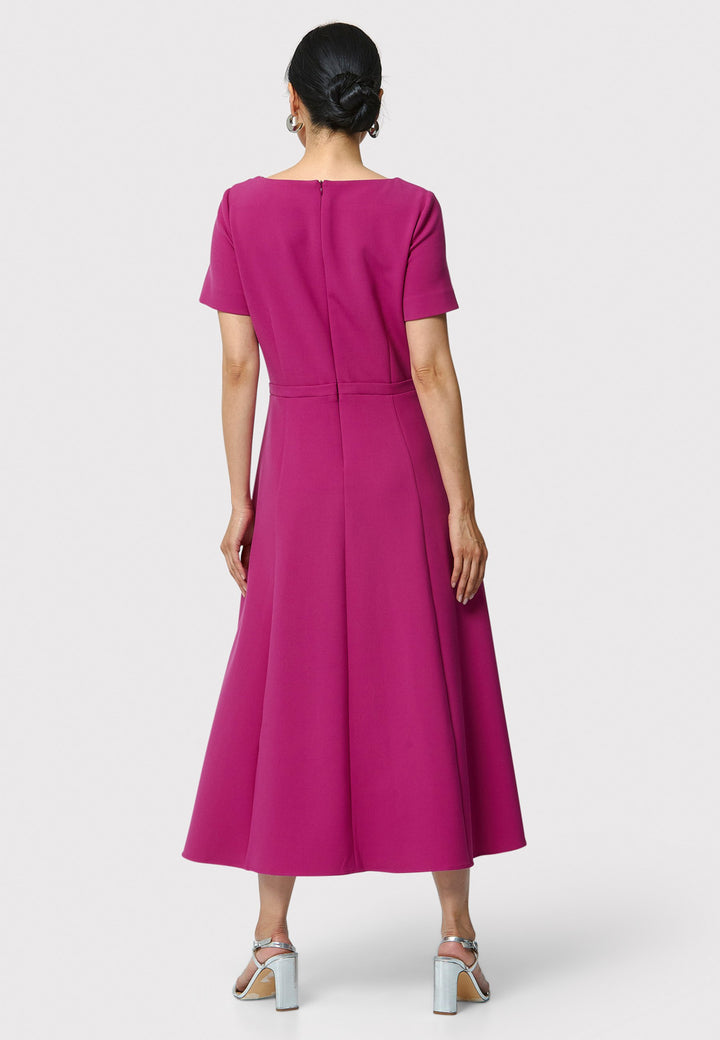 Introducing the Laoise pink dress, a refined statement piece for special occasions. Featuring short sleeves, a fitted bodice, and an elegant shoulder bow detail, this dress has a flattering A-line shape with a cascading paneled skirt. Designed with side seam pockets and a back zip for ease, it combines comfort and sophistication, making it perfect for races, weddings and formal events.