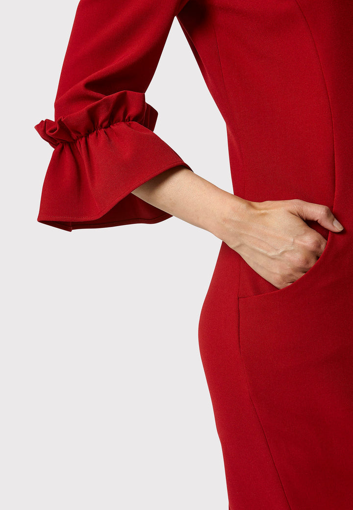 The Maisie Garnet Red Dress, impeccably tailored from signature tricotine fabric with a hint of stretch. This body-skimming silhouette features a round neck and bracelet-length sleeves complemented by exaggerated frill cuffs, ideal for evening cocktails, a night at the theatre, or a stylish winter wedding.