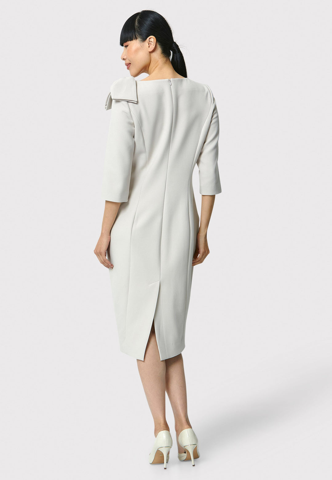 The Natalie dress, crafted from a stone hued tricotine fabric with a hint of stretch, this figure-hugging dress showcases a chic slash neckline, bow detailing, and a mid-calf pencil skirt. Suitable for a night out with friends, a romantic date, or a winter wedding.