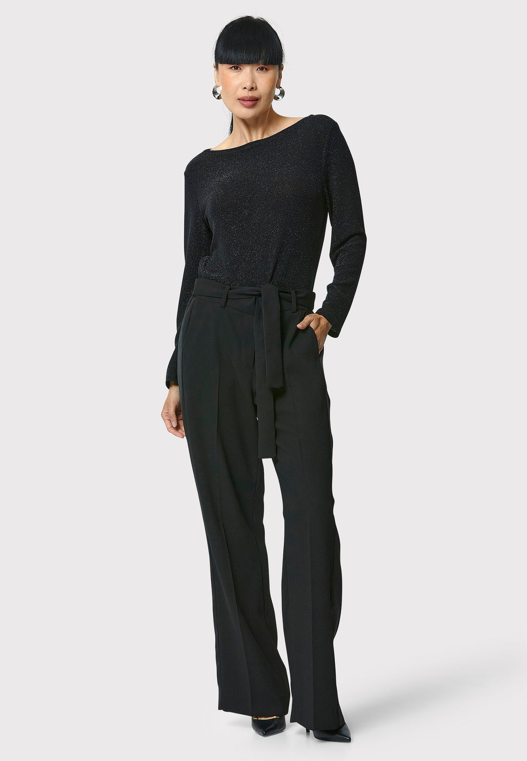 Introducing the Roxanne Black Shimmer Top, an updated version of the beloved best-selling faux-wrap top. This season's design features a beautifully draped neckline for an elegant touch. With its hip-length cut and full-length sleeves, this top combines comfort and chic style effortlessly. Crafted from a black sparkly jersey fabric, it adds a touch of glamour to any outfit. Embrace the ultimate in comfortable chic with the Roxanne Black Shimmer Top.