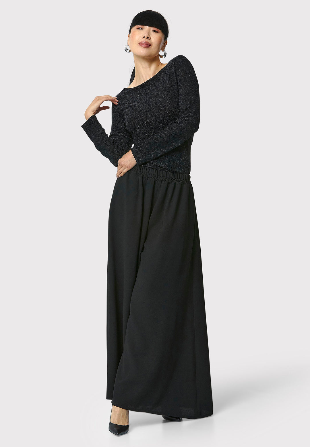 Introducing the Roxanne Black Shimmer Top, an updated version of the beloved best-selling faux-wrap top. This season's design features a beautifully draped neckline for an elegant touch. With its hip-length cut and full-length sleeves, this top combines comfort and chic style effortlessly. Crafted from a black sparkly jersey fabric, it adds a touch of glamour to any outfit. Embrace the ultimate in comfortable chic with the Roxanne Black Shimmer Top.