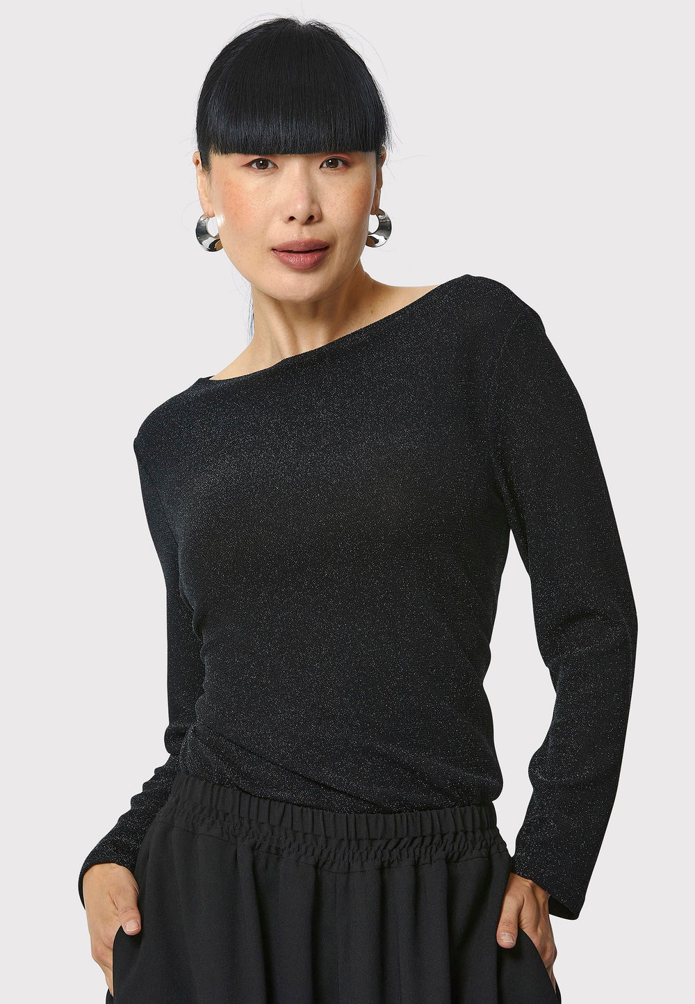 Introducing the Roxanne Black Shimmer Top, an updated version of the beloved best-selling faux-wrap top. This season's design features a beautifully draped neckline for an elegant touch. With its hip-length cut and full-length sleeves, this top combines comfort and chic style effortlessly. Crafted from a black sparkly jersey fabric, it adds a touch of glamour to any outfit. Embrace the ultimate in comfortable chic with the Roxanne Black Shimmer Top.
