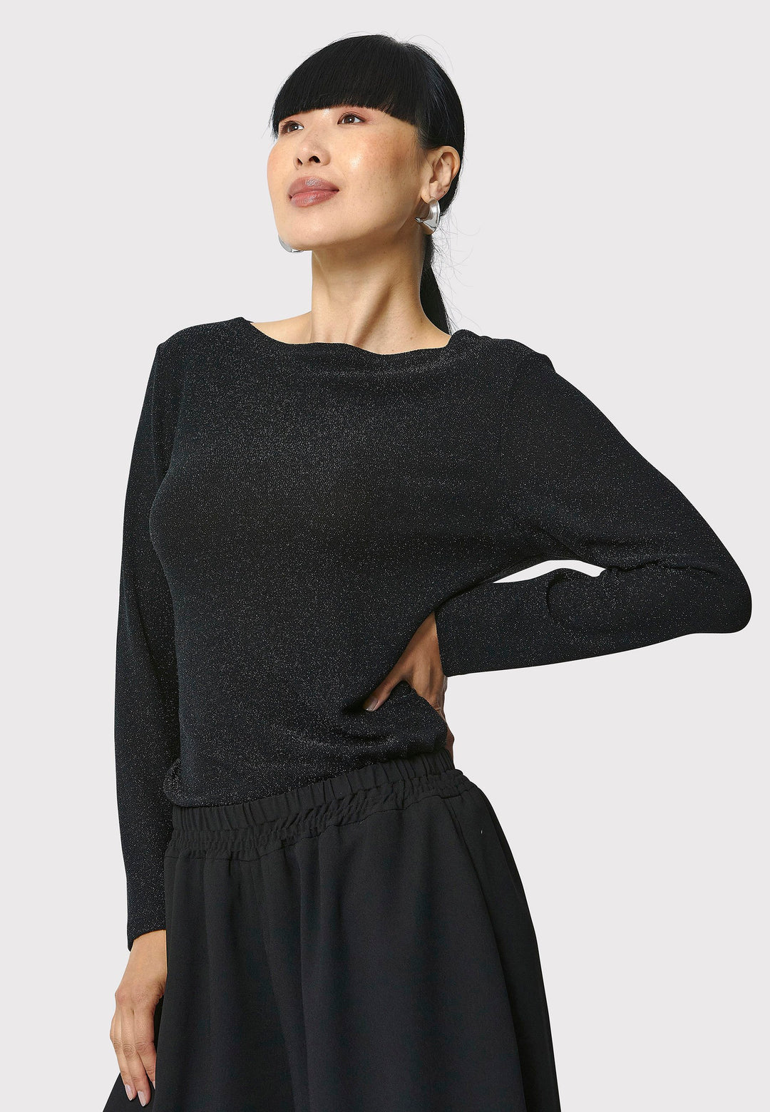 Introducing the Roxanne Black Shimmer Top, an updated version of the beloved best-selling faux-wrap top. This season's design features a beautifully draped neckline for an elegant touch. With its hip-length cut and full-length sleeves, this top combines comfort and chic style effortlessly. Crafted from a black sparkly jersey fabric, it adds a touch of glamour to any outfit. Embrace the ultimate in comfortable chic with the Roxanne Black Shimmer Top.
