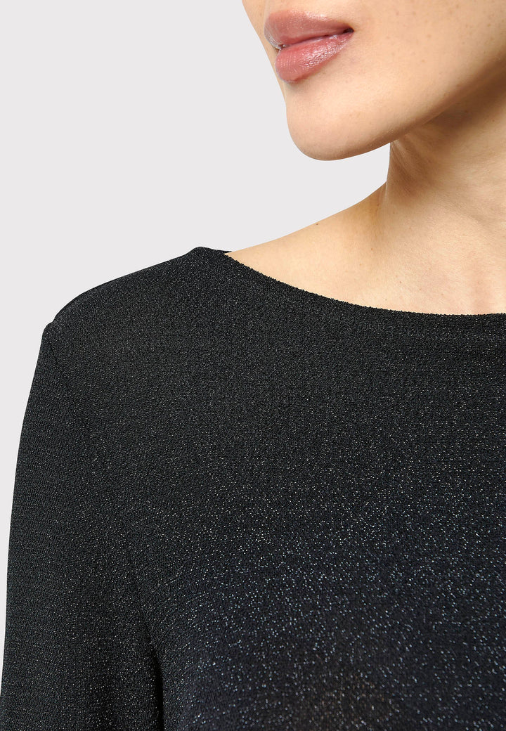 Introducing the Roxanne Black Shimmer Top, an updated version of the beloved best-selling faux-wrap top. This season's design features a beautifully draped neckline for an elegant touch. With its hip-length cut and full-length sleeves, this top combines comfort and chic style effortlessly. Crafted from a black sparkly jersey fabric, it adds a touch of glamour to any outfit. Embrace the ultimate in comfortable chic with the Roxanne Black Shimmer Top.