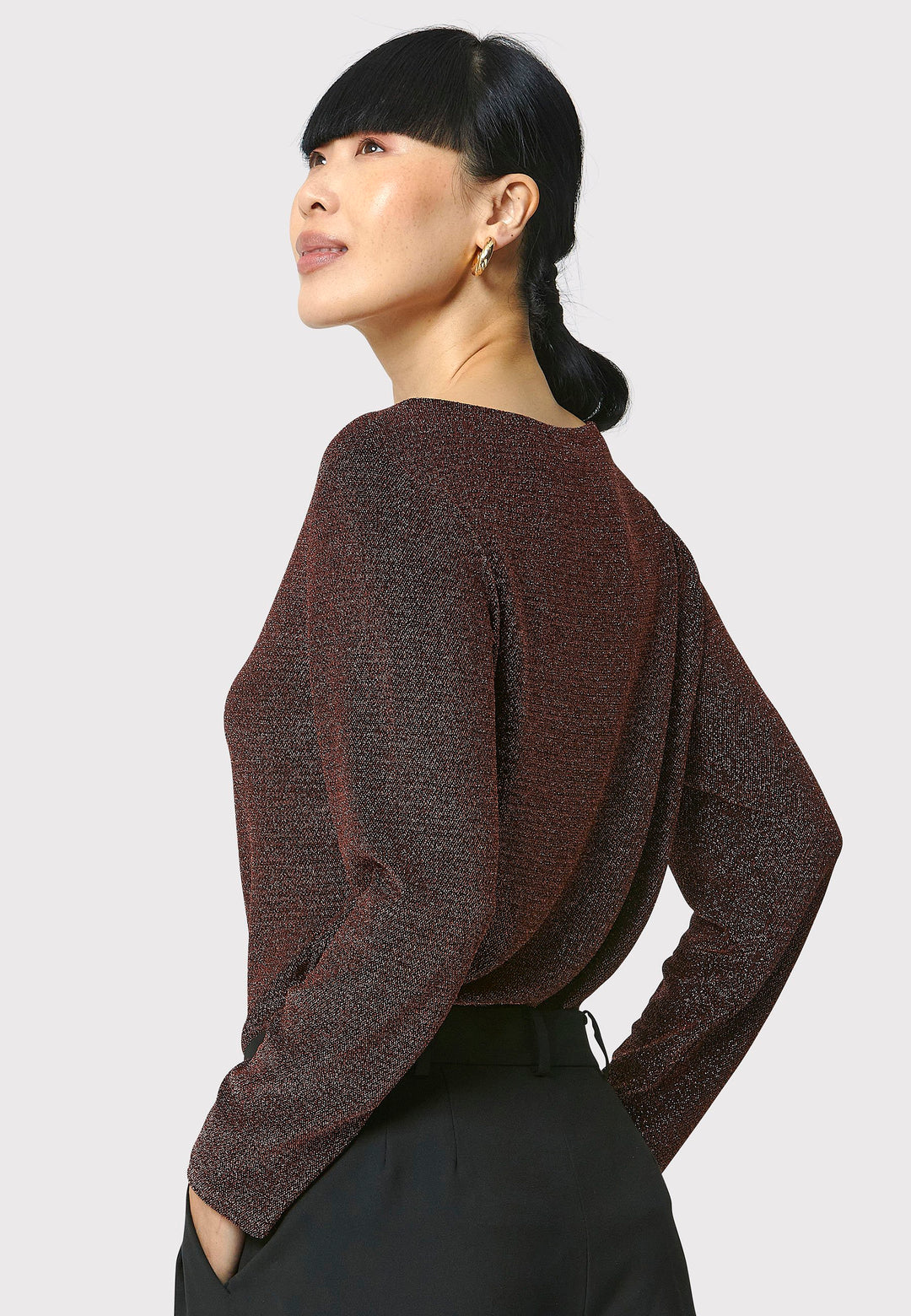 Introducing the Roxanne Copper Shimmer Top, an updated version of the beloved best-selling faux-wrap top. This season's design features a beautifully draped neckline for an elegant touch. With its hip-length cut and full-length sleeves, this top combines comfort and chic style effortlessly. Crafted from a black sparkly jersey fabric, it adds a touch of glamour to any outfit. Embrace the ultimate in comfortable chic with the Roxanne Copper Shimmer Top.