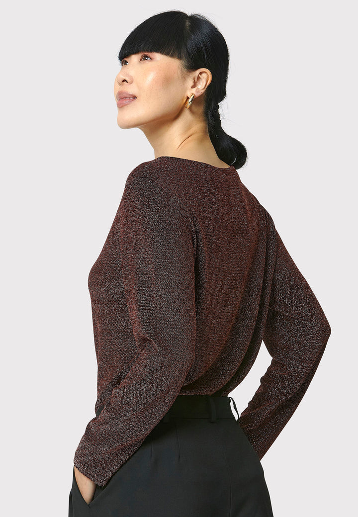 Introducing the Roxanne Copper Shimmer Top, an updated version of the beloved best-selling faux-wrap top. This season's design features a beautifully draped neckline for an elegant touch. With its hip-length cut and full-length sleeves, this top combines comfort and chic style effortlessly. Crafted from a black sparkly jersey fabric, it adds a touch of glamour to any outfit. Embrace the ultimate in comfortable chic with the Roxanne Copper Shimmer Top.