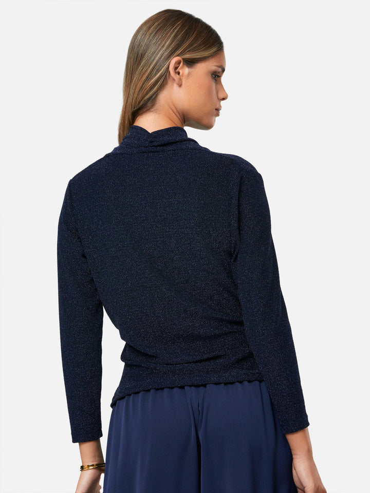 Introducing the Roxanne Midnight Shimmer Top, an updated version of the beloved best-selling faux-wrap top. This season's design features a beautifully draped neckline for an elegant touch. With its hip-length cut and full-length sleeves, this top combines comfort and chic style effortlessly. Crafted from a navy sparkly jersey fabric, it adds a touch of glamour to any outfit. Embrace the ultimate in comfortable chic with the Roxanne Midnight Shimmer Top.