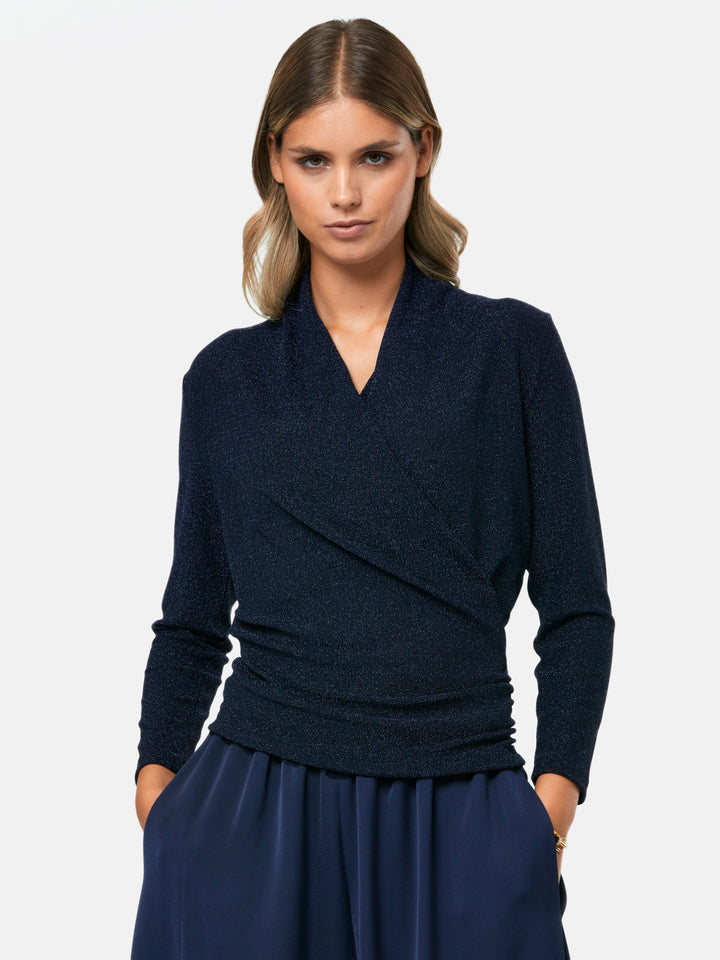 Introducing the Roxanne Midnight Shimmer Top, an updated version of the beloved best-selling faux-wrap top. This season's design features a beautifully draped neckline for an elegant touch. With its hip-length cut and full-length sleeves, this top combines comfort and chic style effortlessly. Crafted from a navy sparkly jersey fabric, it adds a touch of glamour to any outfit. Embrace the ultimate in comfortable chic with the Roxanne Midnight Shimmer Top.