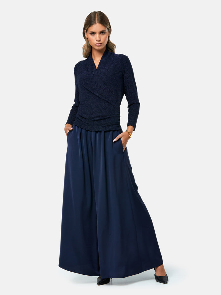 Introducing the Roxanne Midnight Shimmer Top, an updated version of the beloved best-selling faux-wrap top. This season's design features a beautifully draped neckline for an elegant touch. With its hip-length cut and full-length sleeves, this top combines comfort and chic style effortlessly. Crafted from a navy sparkly jersey fabric, it adds a touch of glamour to any outfit. Embrace the ultimate in comfortable chic with the Roxanne Midnight Shimmer Top.