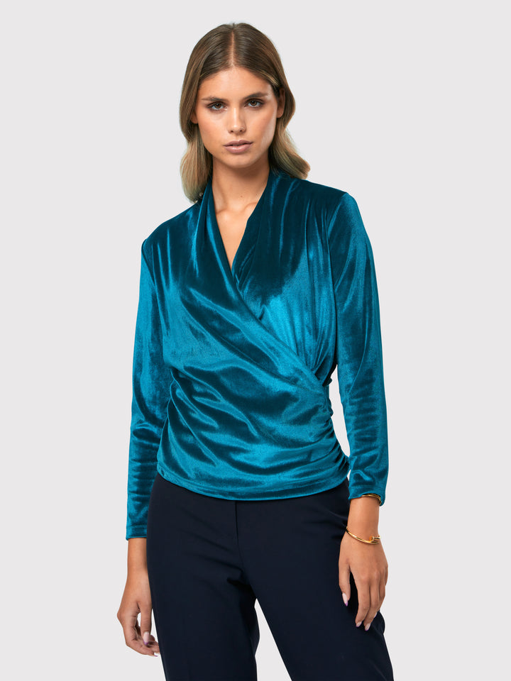 Introducing the Roxanne Petrol Top, an updated version of the beloved best-selling faux-wrap top. This stunning top showcases a sleek silhouette with a gracefully draped v-neckline, creating an air of elegance. Crafted from luxurious stretch velvet in a rich teal tone, it emanates sophistication and allure. The hip-length cut and full-length sleeves offer both comfort and style. Elevate your fashion game with the Roxanne Petrol Top, the epitome of refined chic and a statement piece for any occasion.