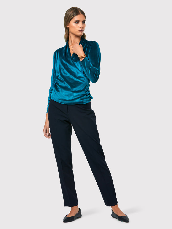 Introducing the Roxanne Petrol Top, an updated version of the beloved best-selling faux-wrap top. This stunning top showcases a sleek silhouette with a gracefully draped v-neckline, creating an air of elegance. Crafted from luxurious stretch velvet in a rich teal tone, it emanates sophistication and allure. The hip-length cut and full-length sleeves offer both comfort and style. Elevate your fashion game with the Roxanne Petrol Top, the epitome of refined chic and a statement piece for any occasion.