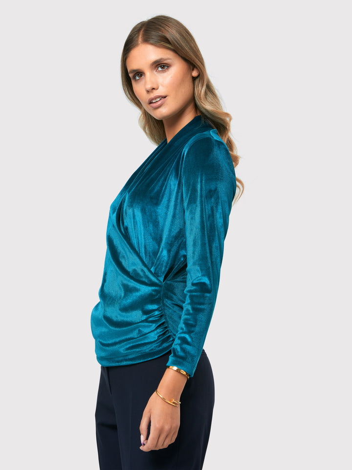 Introducing the Roxanne Petrol Top, an updated version of the beloved best-selling faux-wrap top. This stunning top showcases a sleek silhouette with a gracefully draped v-neckline, creating an air of elegance. Crafted from luxurious stretch velvet in a rich teal tone, it emanates sophistication and allure. The hip-length cut and full-length sleeves offer both comfort and style. Elevate your fashion game with the Roxanne Petrol Top, the epitome of refined chic and a statement piece for any occasion.