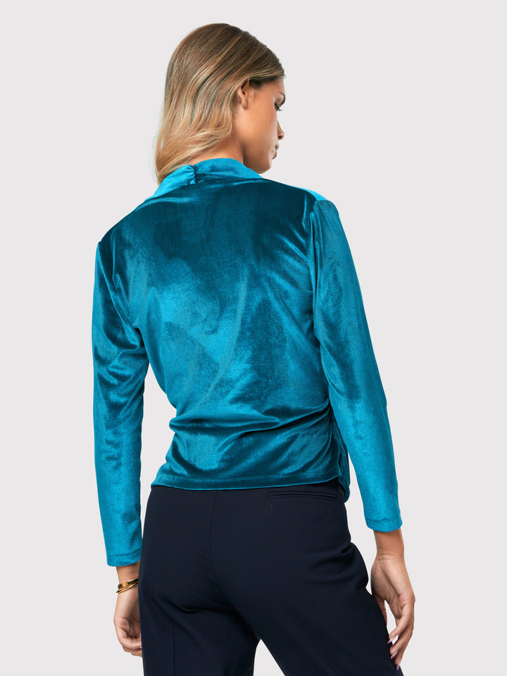 Introducing the Roxanne Petrol Top, an updated version of the beloved best-selling faux-wrap top. This stunning top showcases a sleek silhouette with a gracefully draped v-neckline, creating an air of elegance. Crafted from luxurious stretch velvet in a rich teal tone, it emanates sophistication and allure. The hip-length cut and full-length sleeves offer both comfort and style. Elevate your fashion game with the Roxanne Petrol Top, the epitome of refined chic and a statement piece for any occasion.