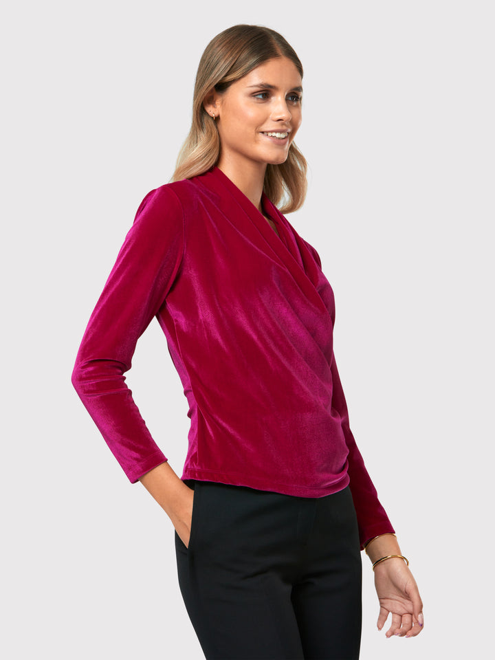 Introducing the Roxanne Fuchsia Velvet Top, an updated version of the beloved best-selling faux-wrap top. This captivating top boasts a sleek silhouette and a beautifully draped v-neckline, adding an elegant touch to your ensemble. Crafted from luxurious fuchsia stretch velvet, it radiates opulence and allure. With its hip-length cut and full-length sleeves, this top effortlessly combines comfort and style.