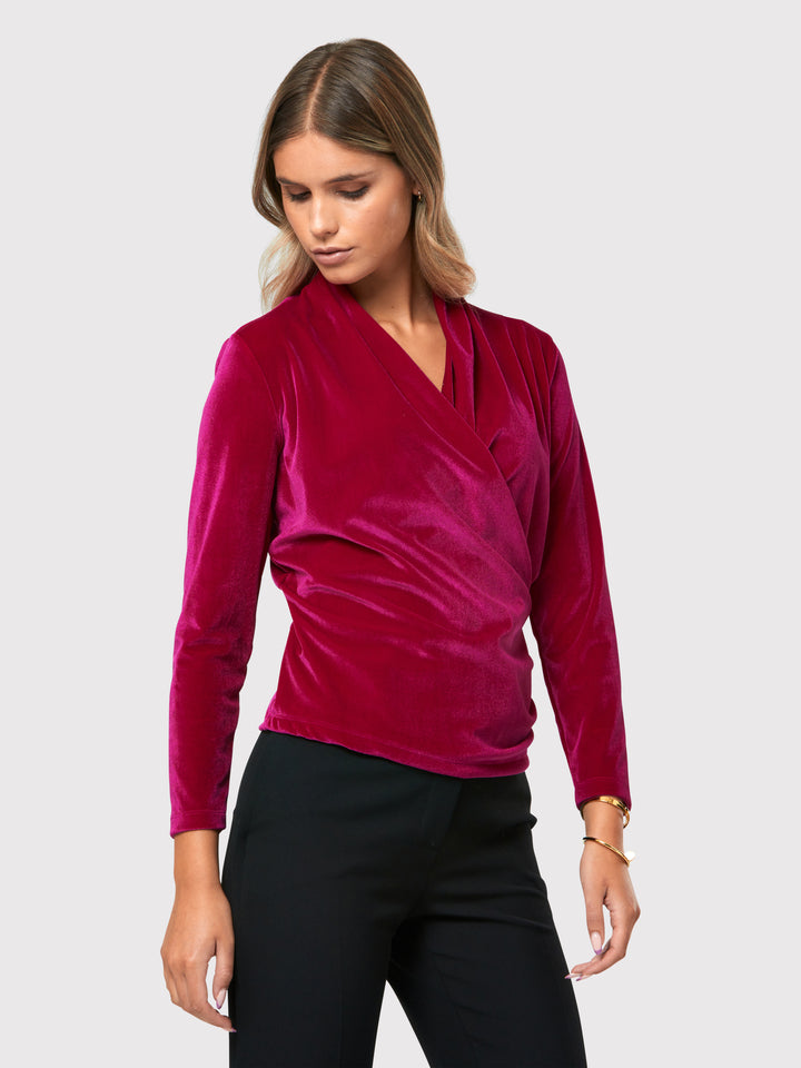 Introducing the Roxanne Fuchsia Velvet Top, an updated version of the beloved best-selling faux-wrap top. This captivating top boasts a sleek silhouette and a beautifully draped v-neckline, adding an elegant touch to your ensemble. Crafted from luxurious fuchsia stretch velvet, it radiates opulence and allure. With its hip-length cut and full-length sleeves, this top effortlessly combines comfort and style.