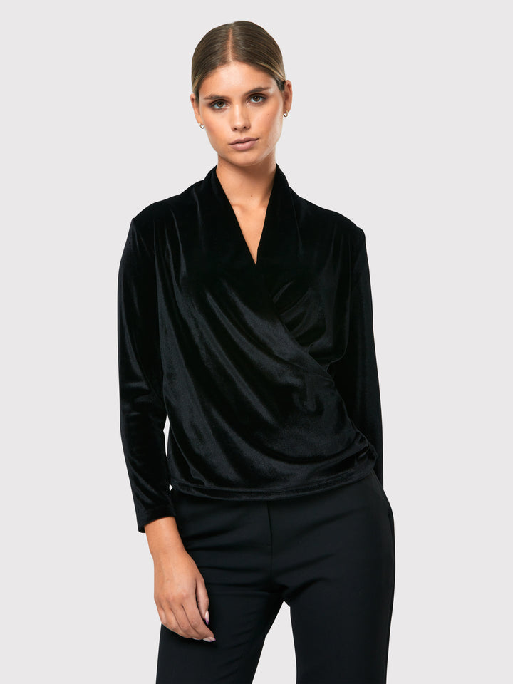 Introducing the Roxanne Black Velvet Top, an updated version of the beloved best-selling faux-wrap topc This exquisite top features a sleek silhouette with a beautifully draped V-neckline, adding a touch of elegance to any ensemble. Crafted from luxurious black stretch velvet, it exudes sophistication and opulence. With its hip-length cut and full-length sleeves, this top effortlessly combines comfort and style. Elevate your wardrobe with the Roxanne Black Velvet Top, the epitome of refined chic.