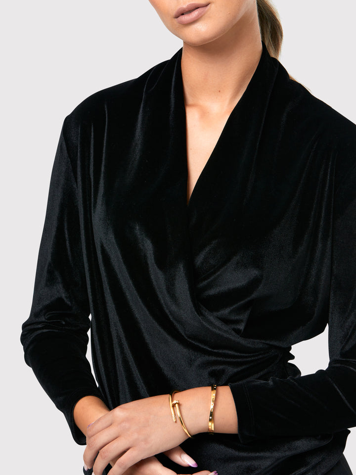 Introducing the Roxanne Black Velvet Top, an updated version of the beloved best-selling faux-wrap topc This exquisite top features a sleek silhouette with a beautifully draped V-neckline, adding a touch of elegance to any ensemble. Crafted from luxurious black stretch velvet, it exudes sophistication and opulence. With its hip-length cut and full-length sleeves, this top effortlessly combines comfort and style. Elevate your wardrobe with the Roxanne Black Velvet Top, the epitome of refined chic.